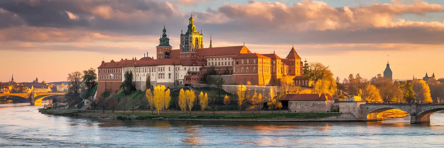 Wawel Royal Castle rising above the Vistula River in Kraków at golden hour with autumn trees along the riverbank
