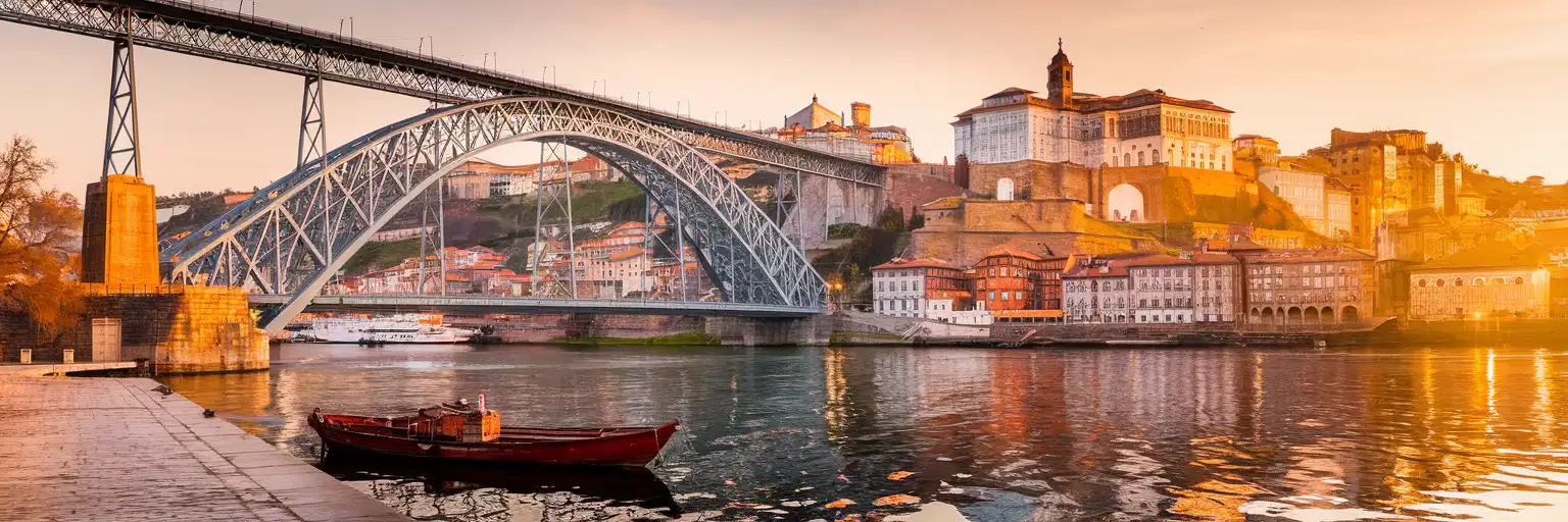Dom Luís I Bridge spanning the Douro River at golden hour with Porto's Ribeira district and traditional rabelo boats
