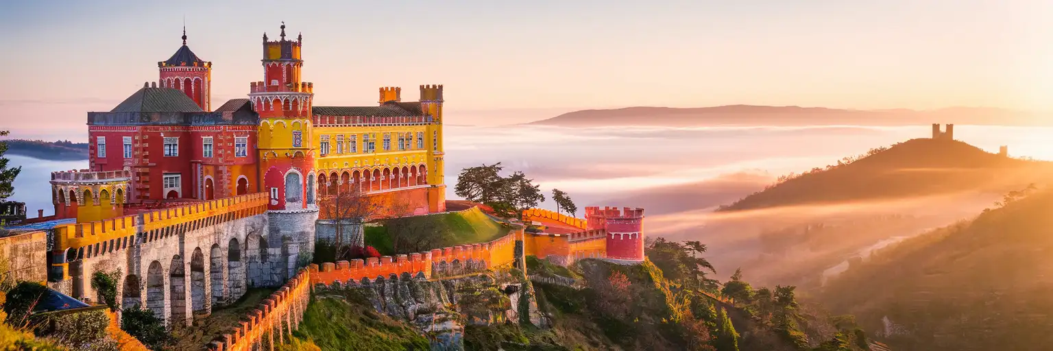 Pena Palace rising above the forested Sintra Mountains at golden hour with morning mist in the valleys below