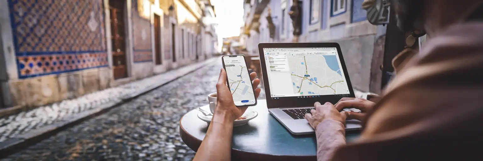 Podróżnik korzystający ze smartfona do nawigacji i laptopa w kawiarni na świeżym powietrzu w dzielnicy Alfama w Lizbonie z tradycyjną portugalską architekturą