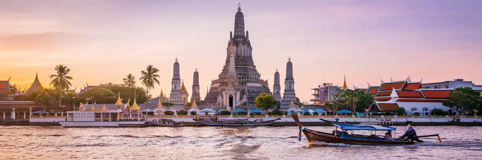 Wat Arun temple rising from the Chao Phraya River at golden hour in Bangkok Thailand