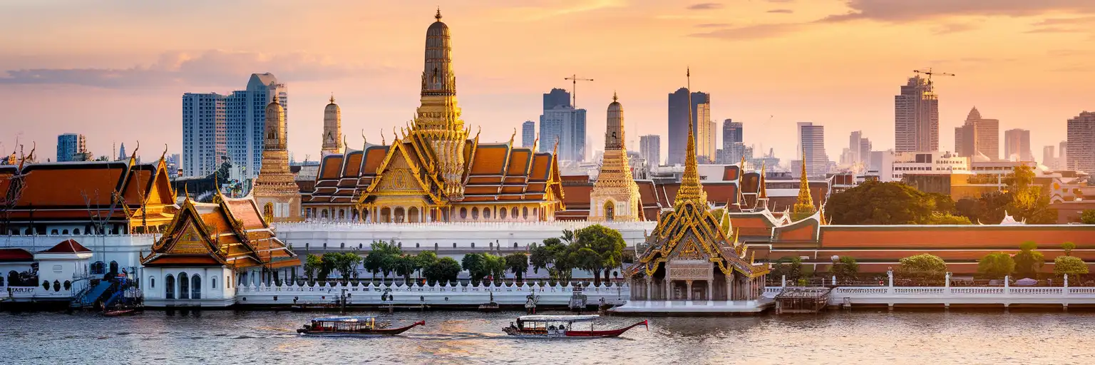 The Grand Palace and Wat Phra Kaew in Bangkok at golden hour with the Chao Phraya River and city skyline
