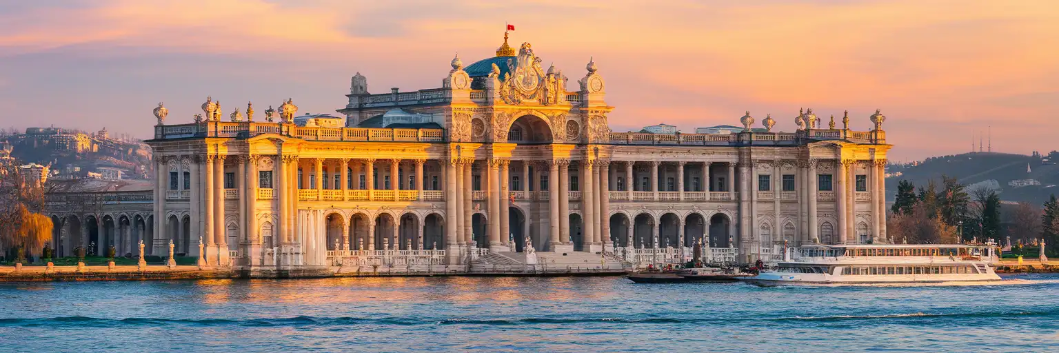 Dolmabahçe Palace waterfront facade viewed from the Bosphorus at golden hour with ferries on the strait