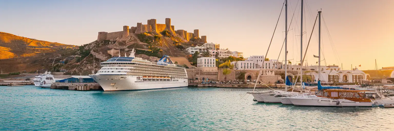 Bodrum Cruise Port waterfront with cruise ships docked and Bodrum Castle on the peninsula at golden hour