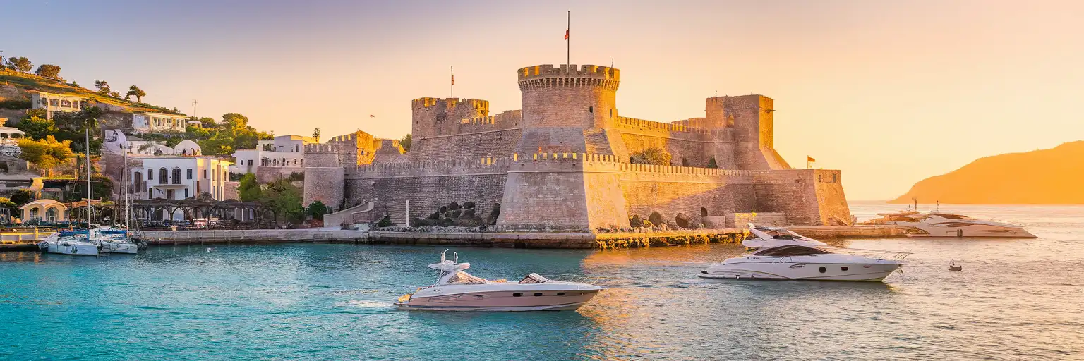 Bodrum Castle rising from the harbor at golden hour with traditional white houses and Aegean Sea in the background