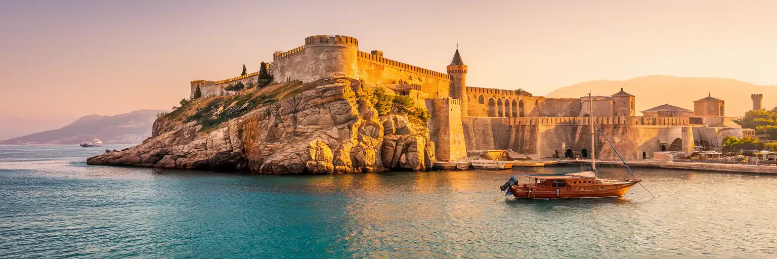 Alanya Castle and Red Tower overlooking the Mediterranean harbor at golden hour with traditional boats in the foreground