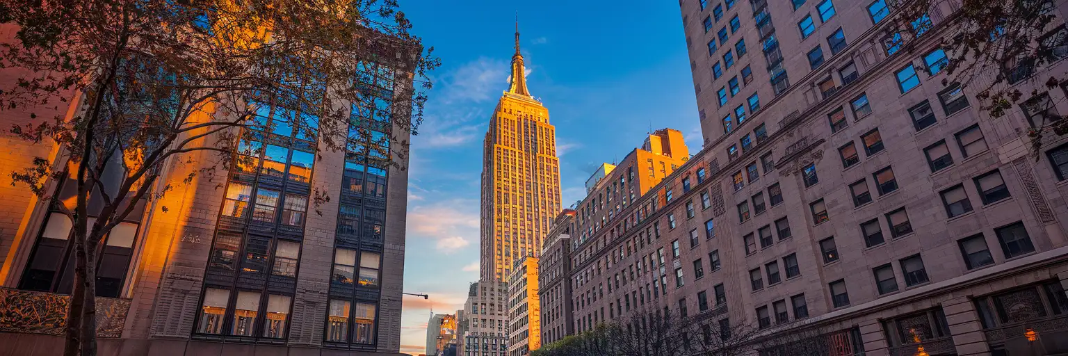 The Empire State Building Art Deco facade rising into the Manhattan sky at golden hour, viewed from Fifth Avenue in Midtown