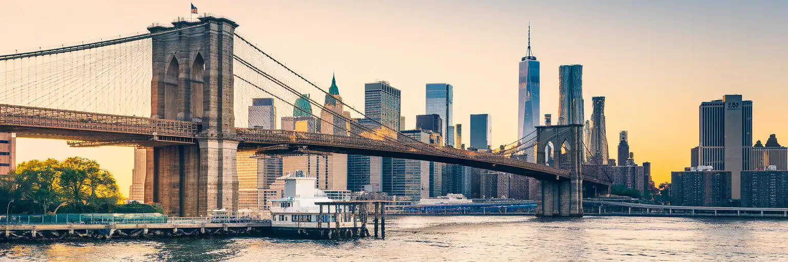 Brooklyn Bridge spanning the East River at golden hour with Manhattan skyline and Gothic stone towers