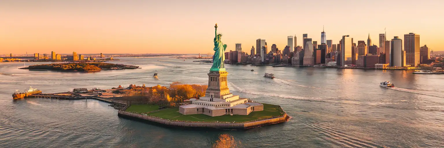 The Statue of Liberty rising from New York Harbor with the Manhattan skyline in the distance at golden hour