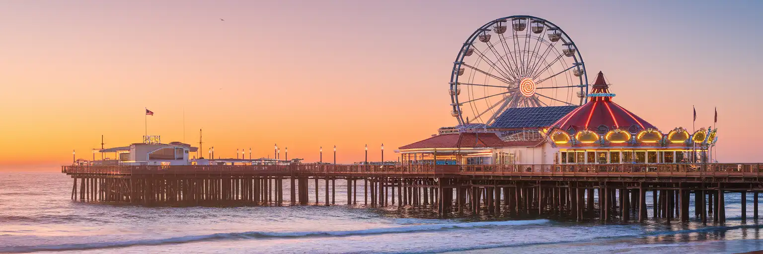 Santa Monica Pier stretching into the Pacific Ocean at golden hour with the Pacific Wheel Ferris wheel and Pacific Park amusements glowing in warm sunset light