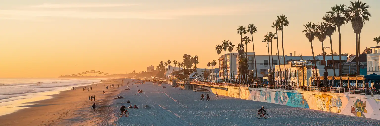 Venice Beach Boardwalk at golden hour with palm trees, colorful art walls, and the Pacific Ocean stretching along the sandy shore