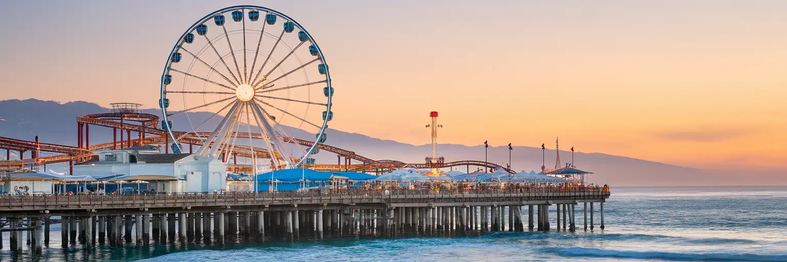 Pacific Park de pe Santa Monica Pier la ora de aur, cu roata Ferris Pacific Wheel și roller coasterul West Coaster pe fundalul apusului din California