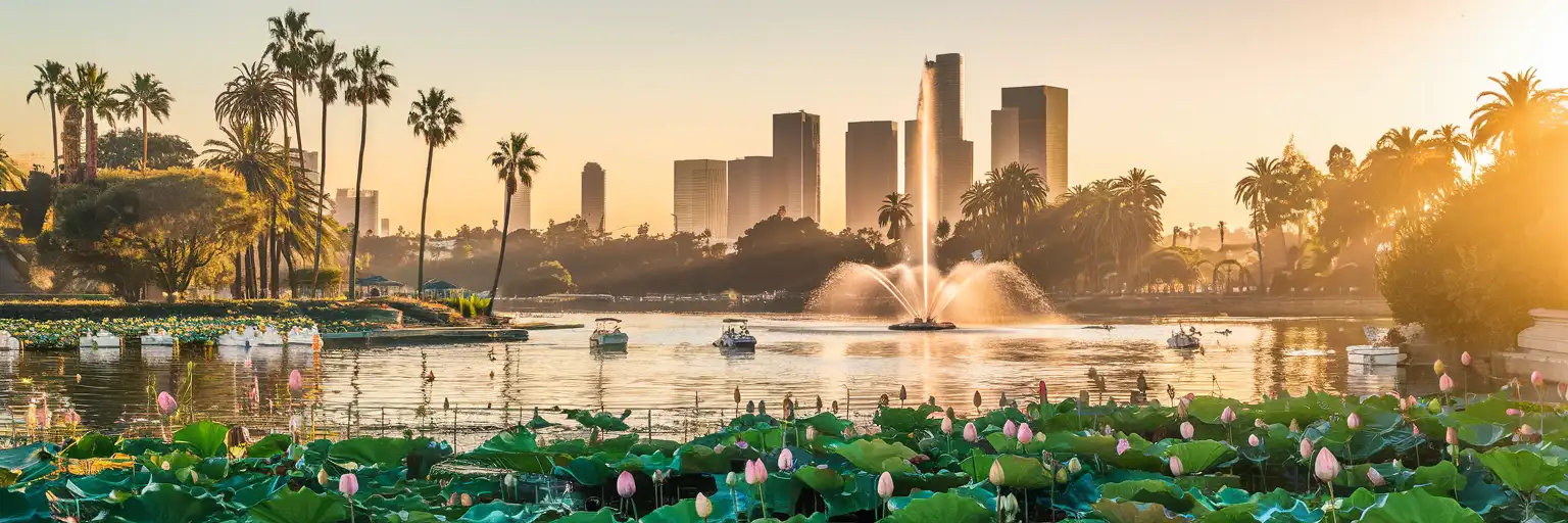 Vista amplia al atardecer de Echo Park Lake con fuente, botes de pedales, palmeras y el horizonte del centro de Los Ángeles al fondo