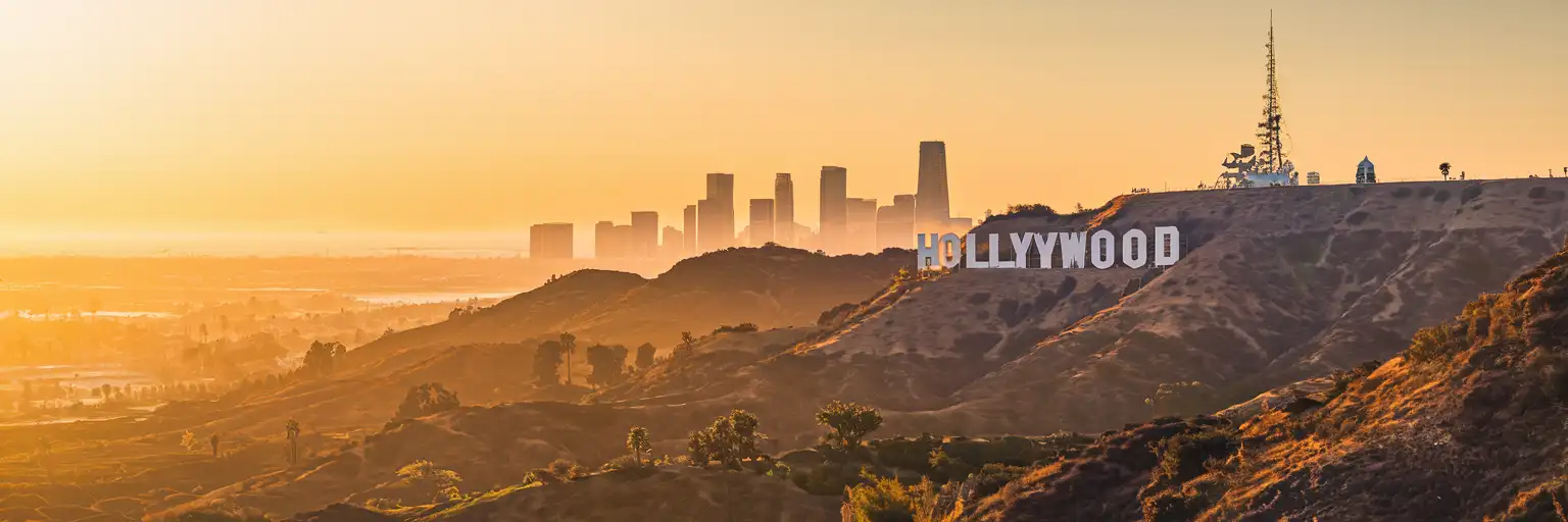 Hollywood Sign on Mount Lee overlooking Los Angeles basin at golden hour with downtown skyline in distance