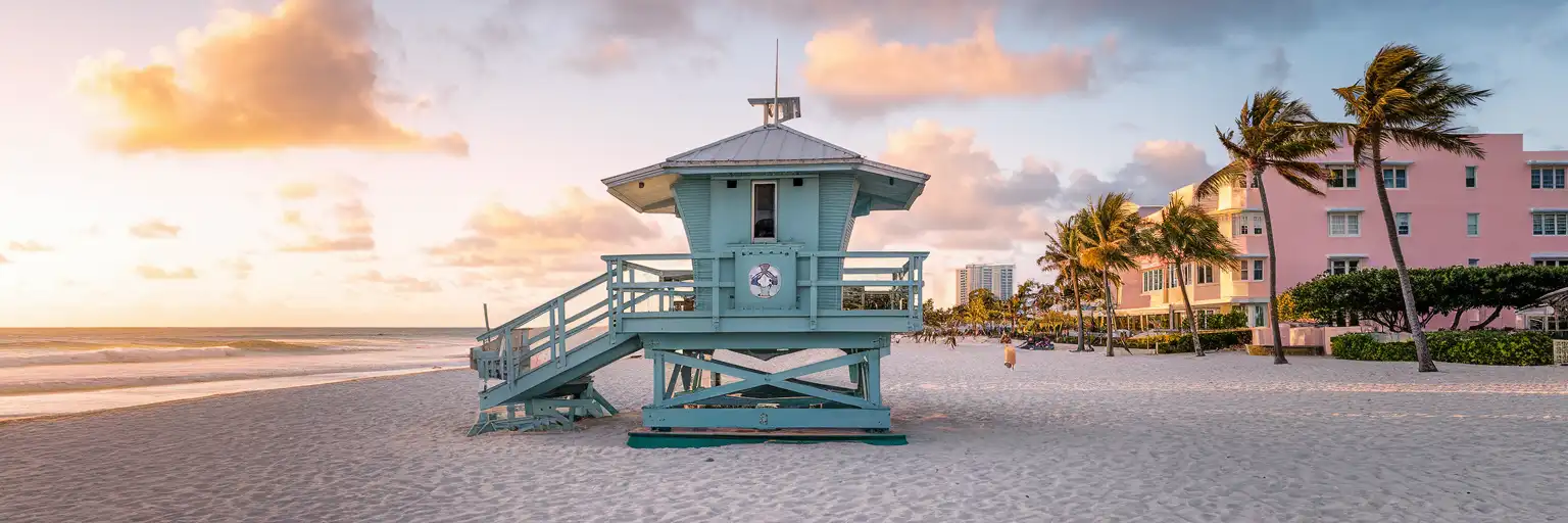 Art Deco lifeguard tower on South Beach Miami with pastel Ocean Drive hotels and palm trees at golden hour sunset