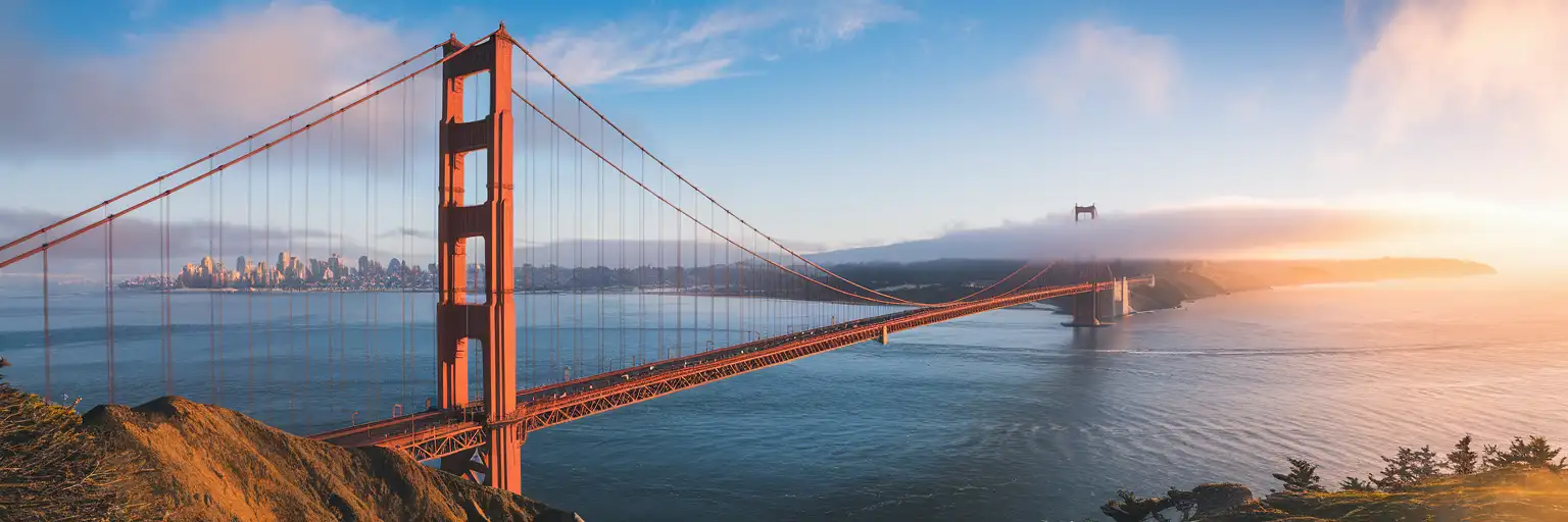 Golden Gate Bridge spanning the Golden Gate strait at golden hour with San Francisco skyline in the background and morning fog wisps around the International Orange towers