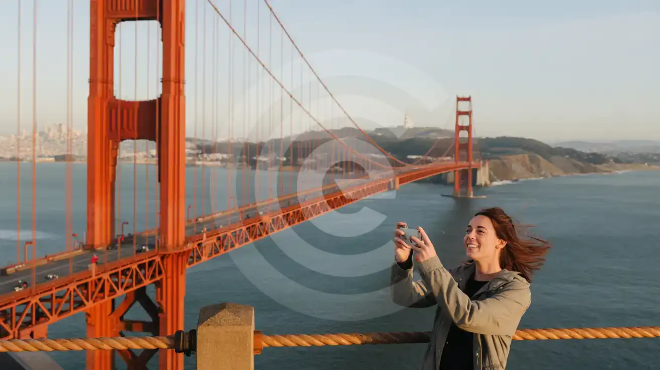 Solo female traveler photographing the view from mid-span on the Golden Gate Bridge pedestrian walkway with Alcatraz Island visible across San Francisco Bay