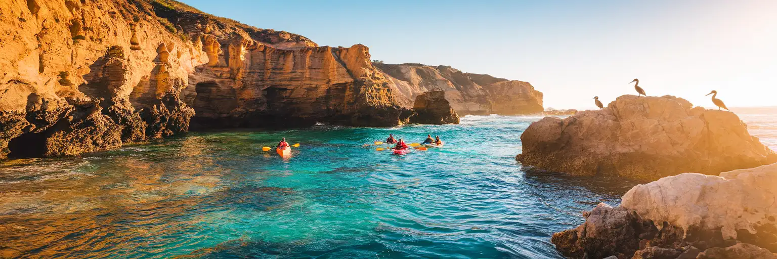 Golden hour view of La Jolla sea caves coastline with kayakers paddling toward sandstone cliff cave openings along the Pacific Ocean