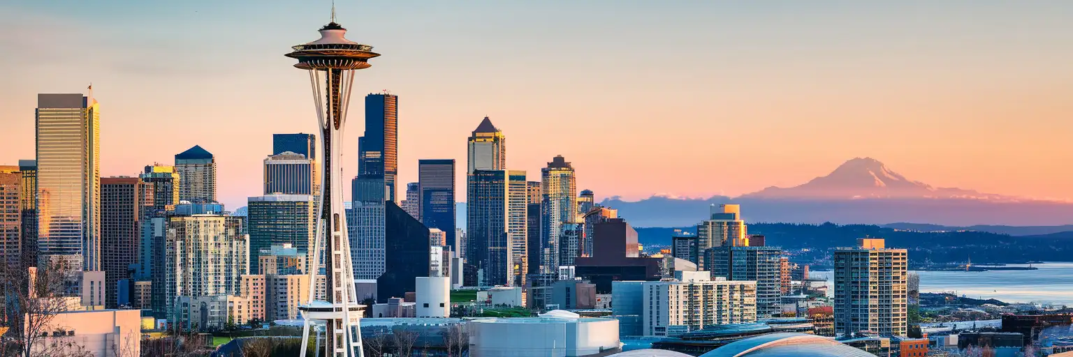 The Space Needle tower rising above Seattle Center at golden hour with Elliott Bay and the Olympic Mountains in the background
