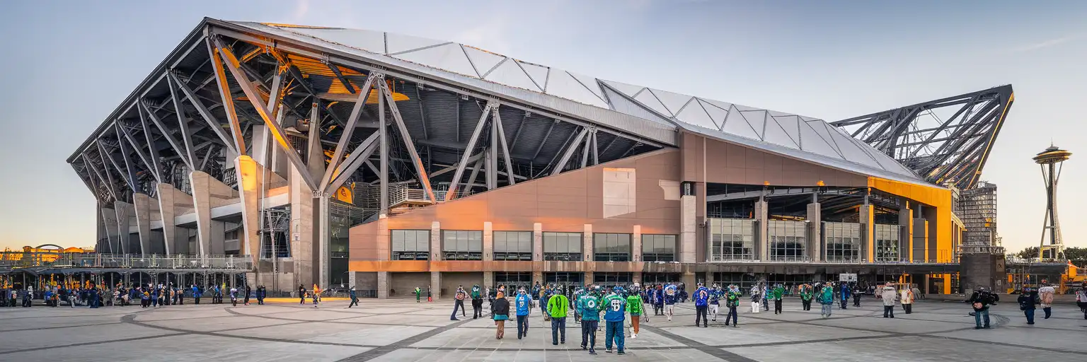 Lumen Field exterior at golden hour with exposed steel trusses and Seattle skyline visible behind the stadium